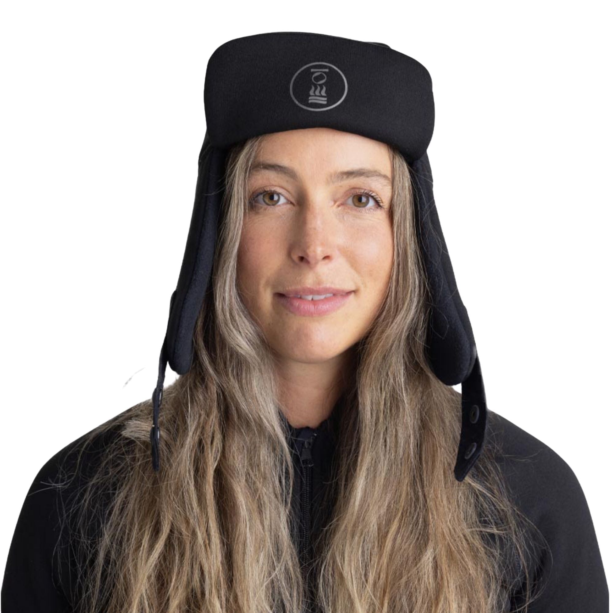 A woman with long blonde hair wearing a black insulated winter trapper hat with ear flaps and a small white circular logo on the front, set against a plain white background.
