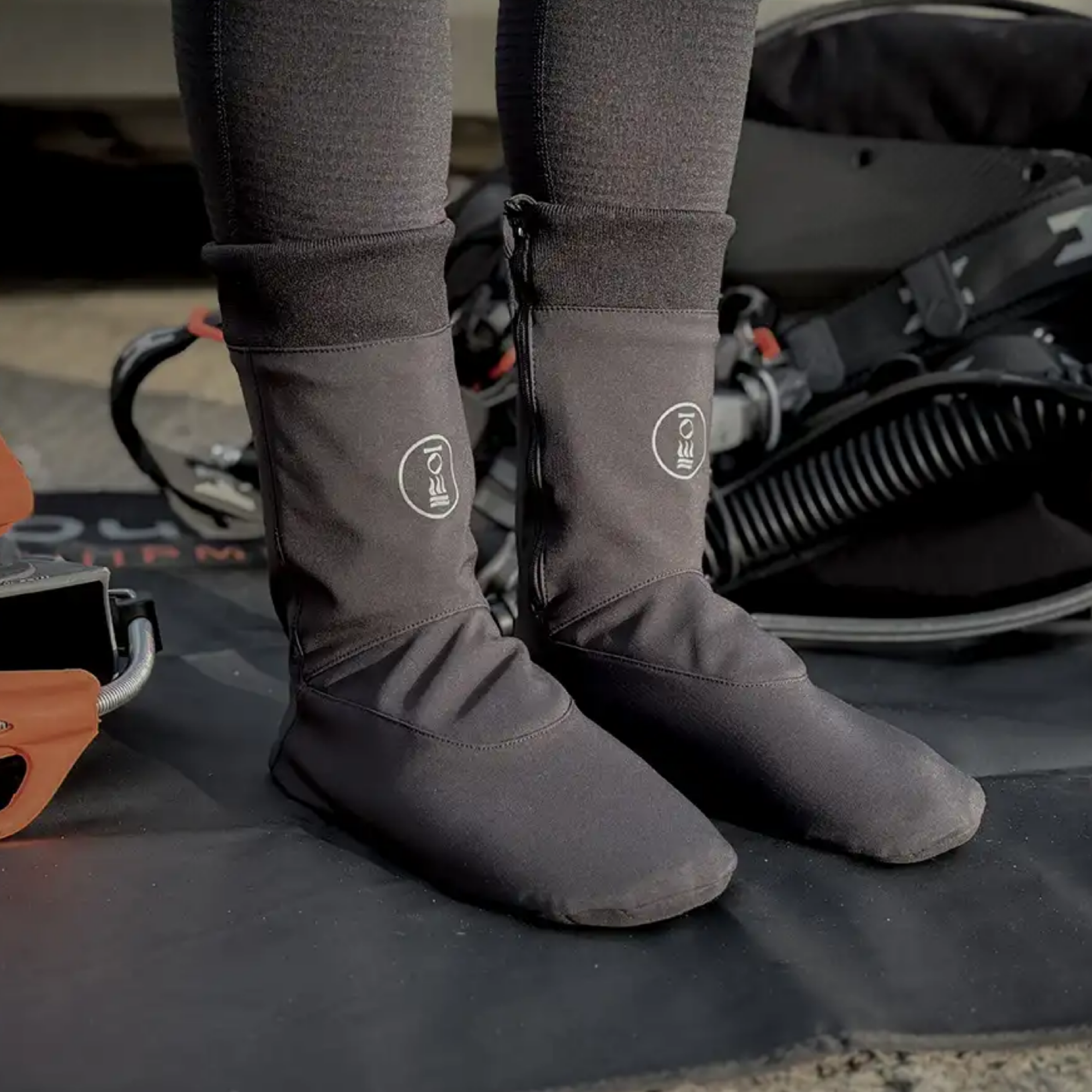 A person wearing dark socks with side zippers, standing on a black mat with equipment in the background.
