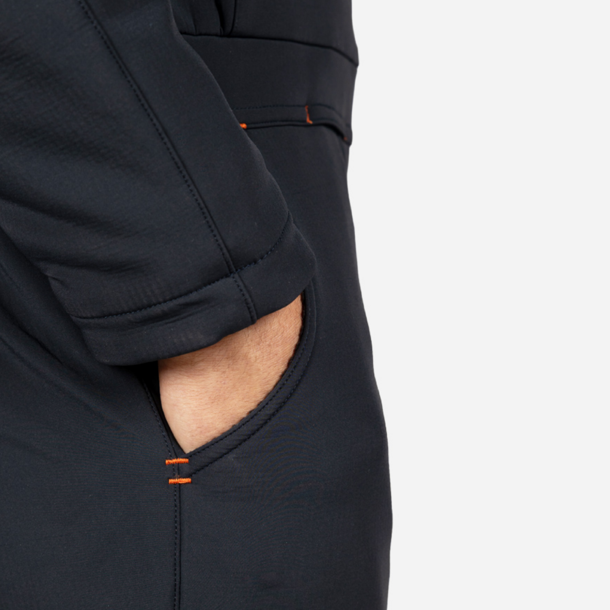 Close-up of a person wearing dark pants with a side pocket and bright orange stitching detail, showing a hand in the pocket.