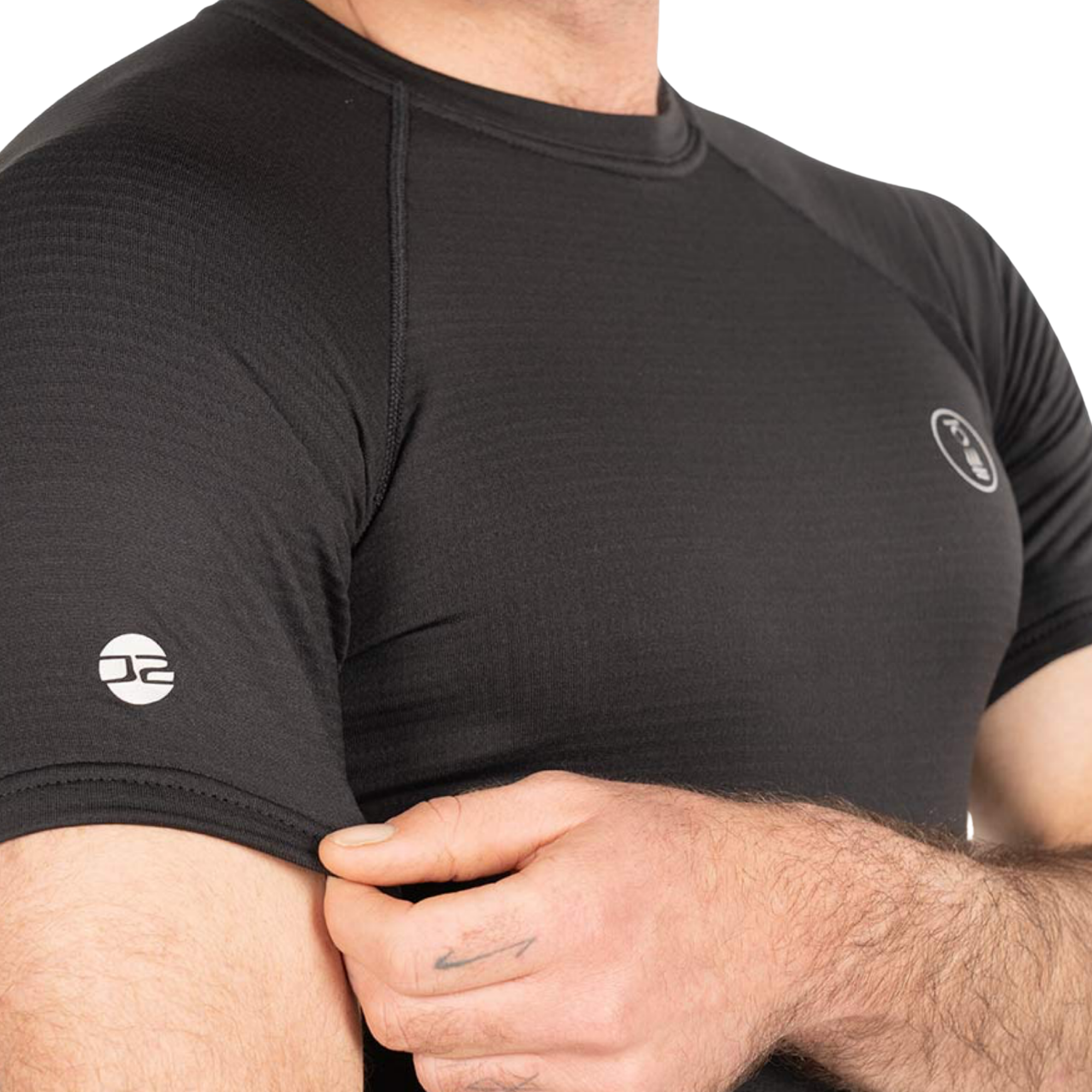 A close-up of a man wearing a black athletic short-sleeve compression shirt with a textured knit fabric and white circular logos on the chest and sleeve.