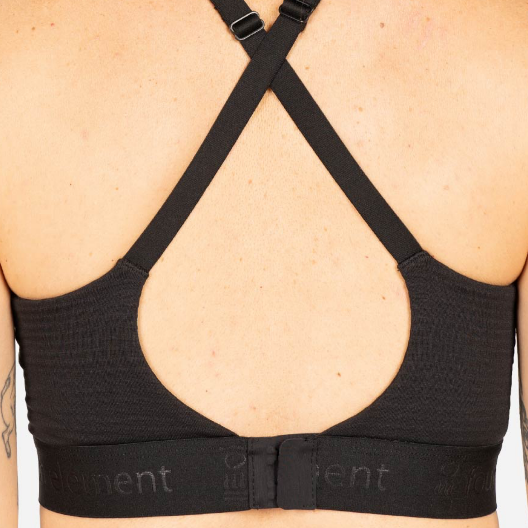 Close-up back view of a black sports bra with crisscross shoulder straps and a wide underband, shown on a model.