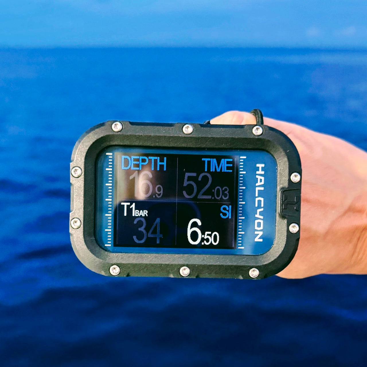 A Halcyon dive computer held by a hand against a vibrant blue ocean background. 
