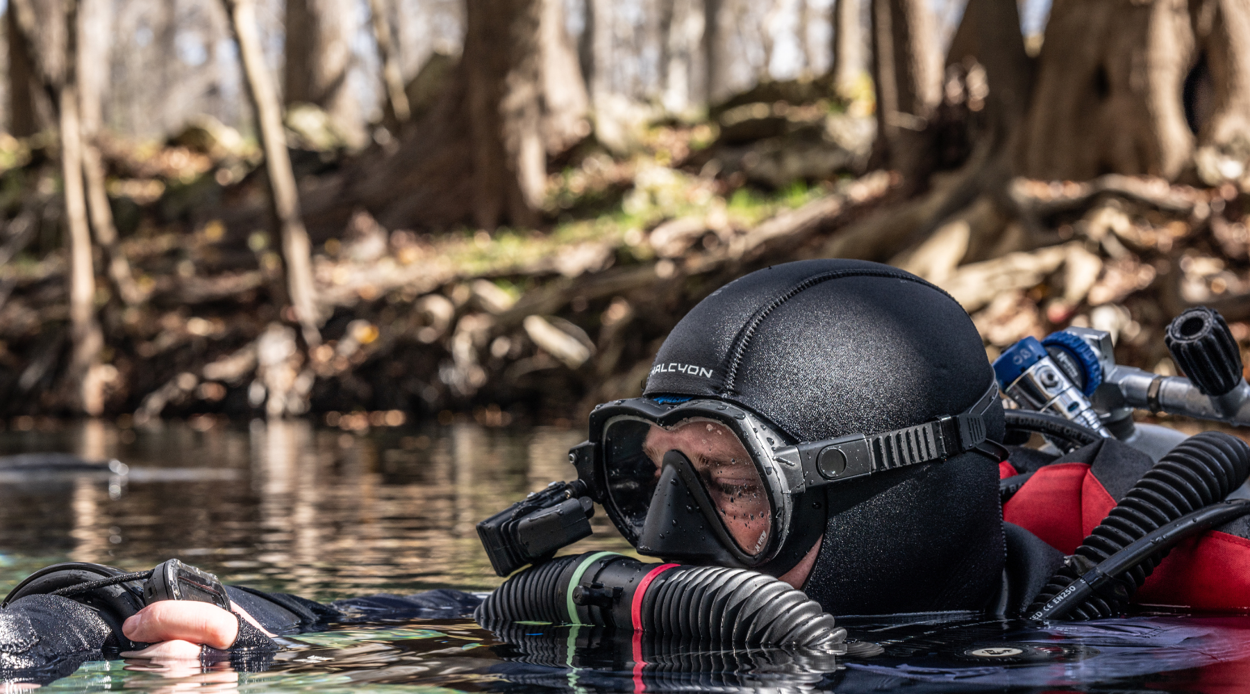 A person in the water with black mask and hood, with Halcyon Symbios Rebreather 