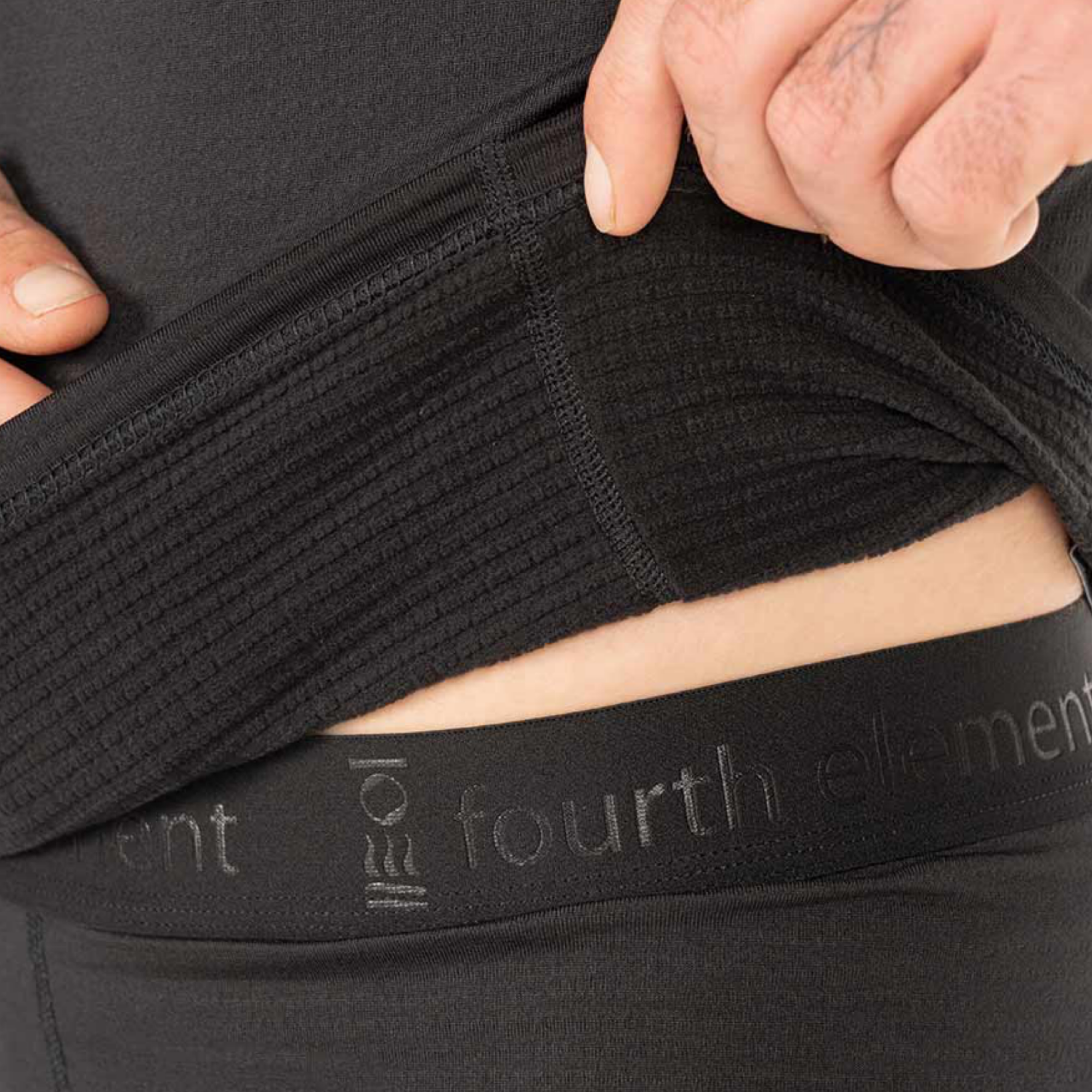 Close-up of a person lifting a black ribbed compression garment or support panel over their lower torso, with the waistband showing the text 'fourth element' and a small logo.